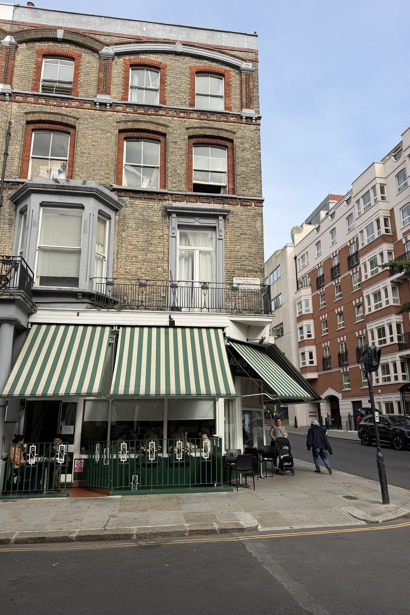 Café en terrasse sous un auvent rayé vert et blanc, immeuble en brique