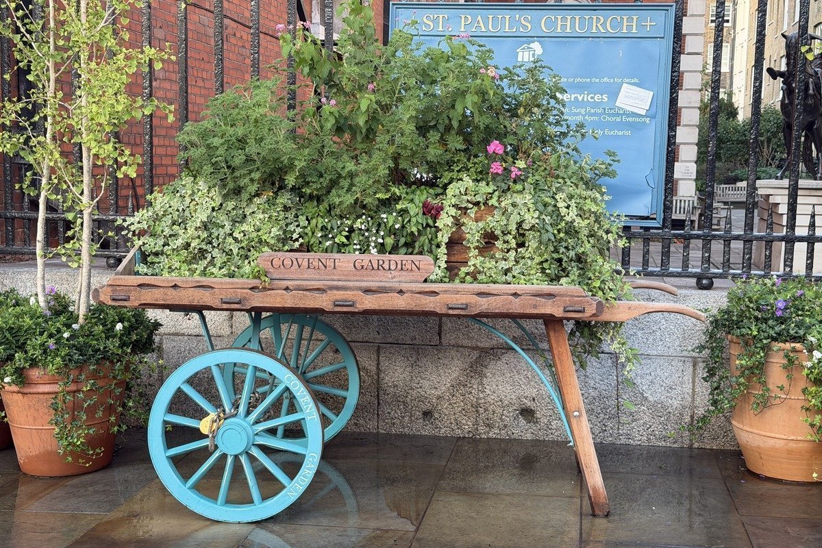 Ancienne charrette en bois ornée de plantes fleuries devant une église