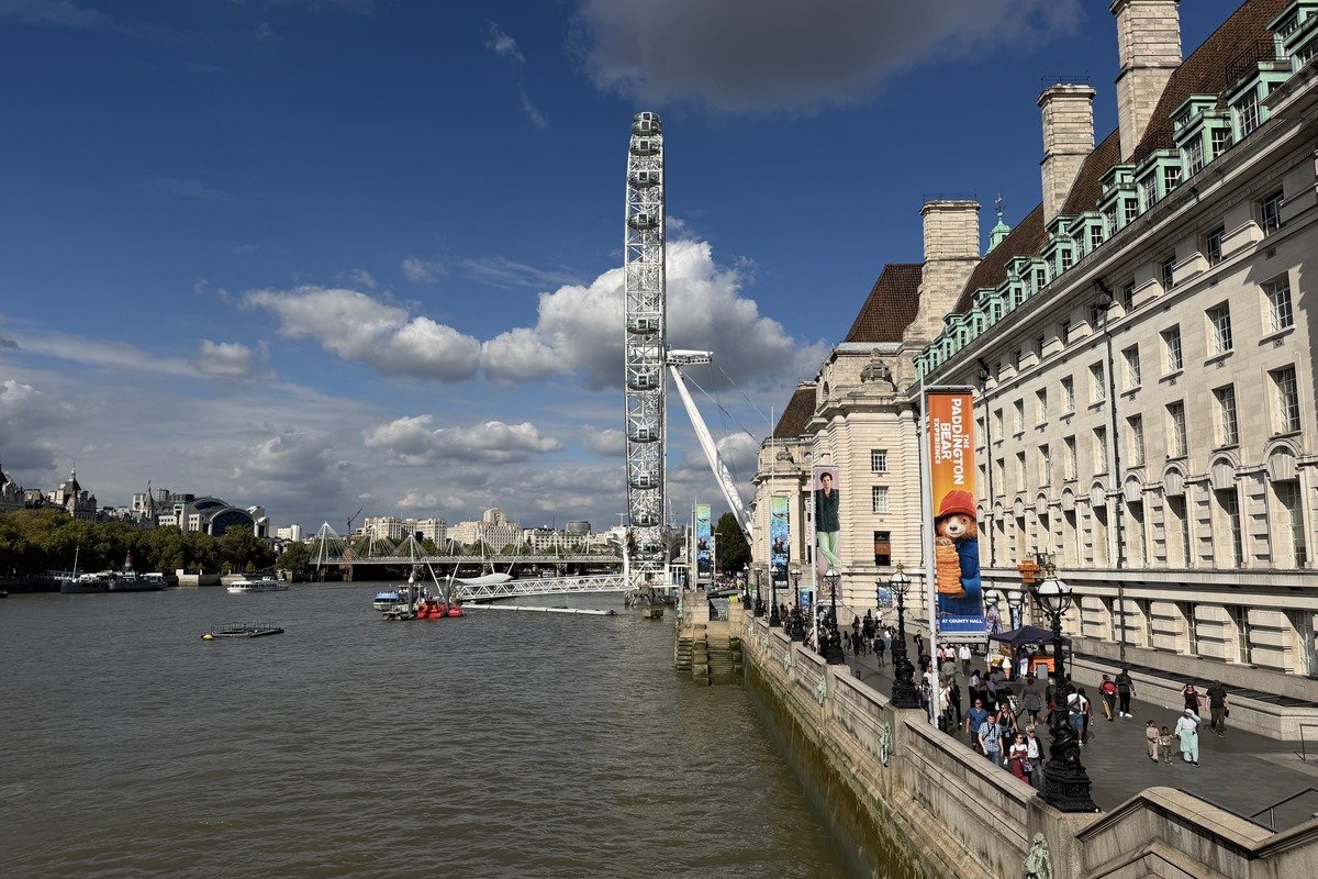 Grande roue blanche au bord d'un fleuve avec bâtiment classique et promeneurs