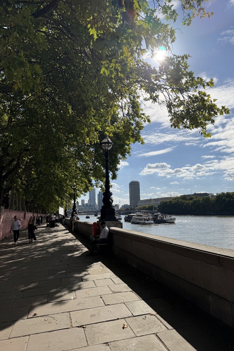 Promenade ombragée au bord d'une rivière avec lampadaire victorien et passants