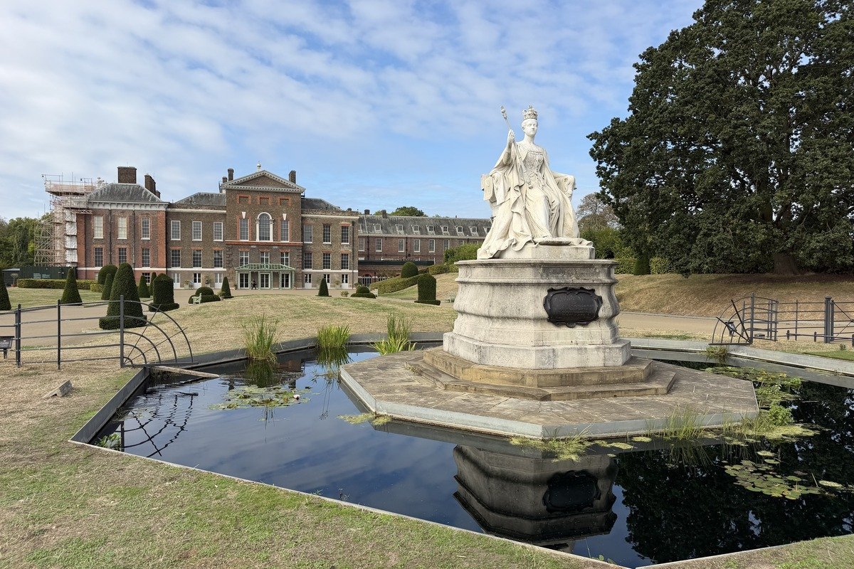 Statue de reine couronnée devant un palais en brique rouge et bassin