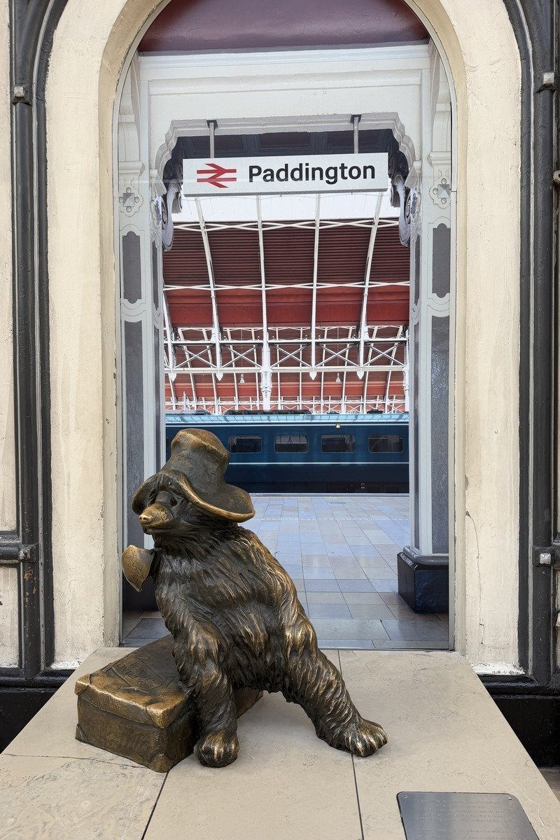 Statue en bronze d'un ours avec chapeau et valise devant une arche de gare