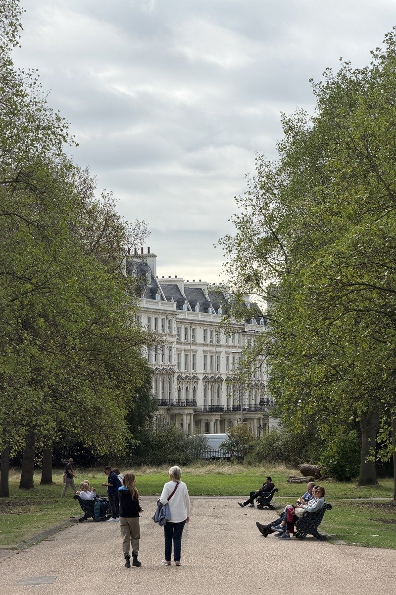 Allée de parc bordée d'arbres avec promeneurs et façade blanche