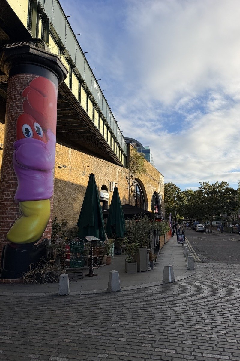 Sculpture colorée sur pilier sous viaduc ferroviaire avec terrasse de restaurant