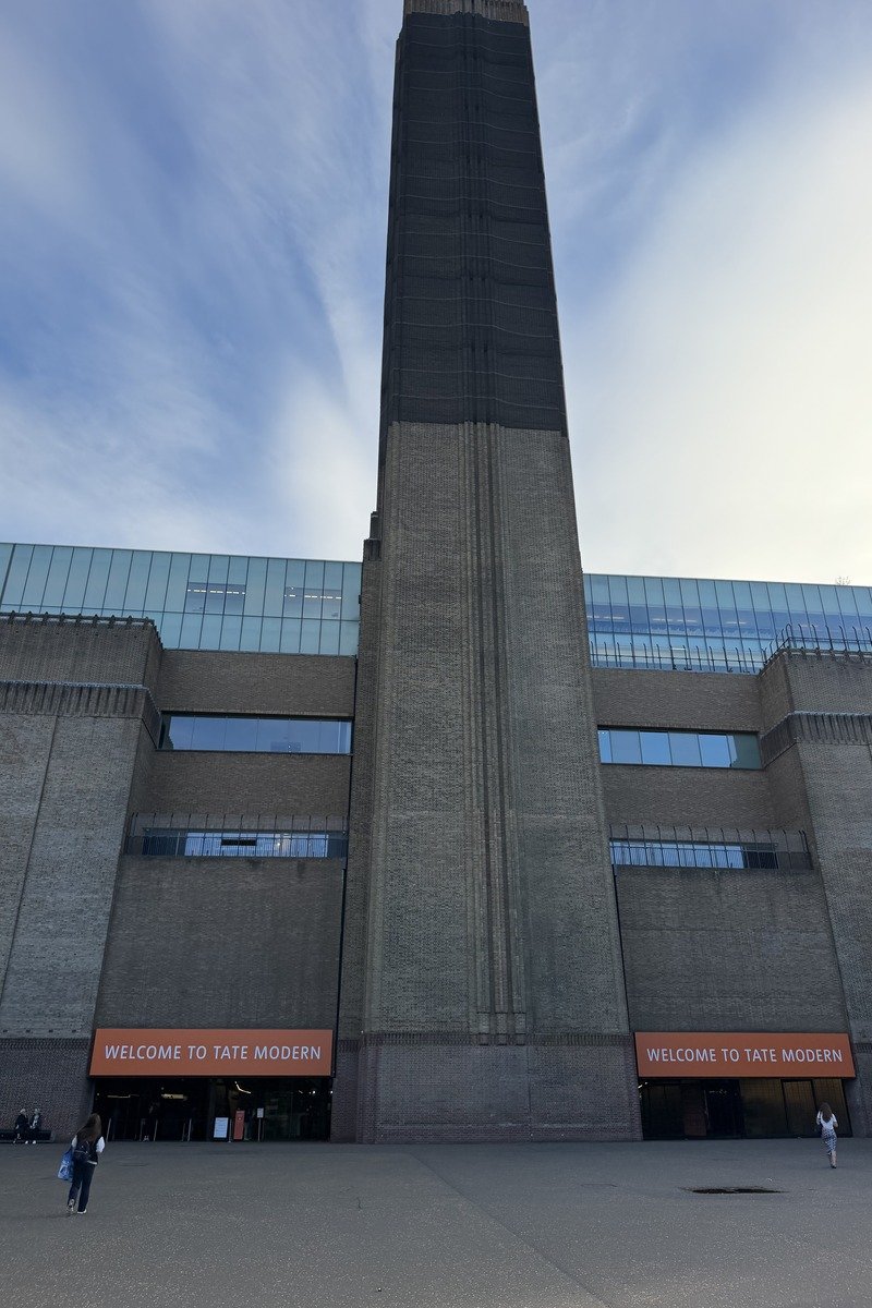 Façade en brique d'un musée avec haute cheminée et panneaux orange d'accueil