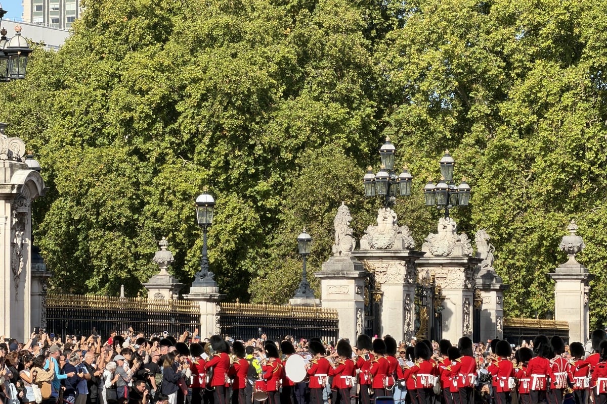 Fanfare de gardes en uniforme rouge défilant devant une grille ornementale