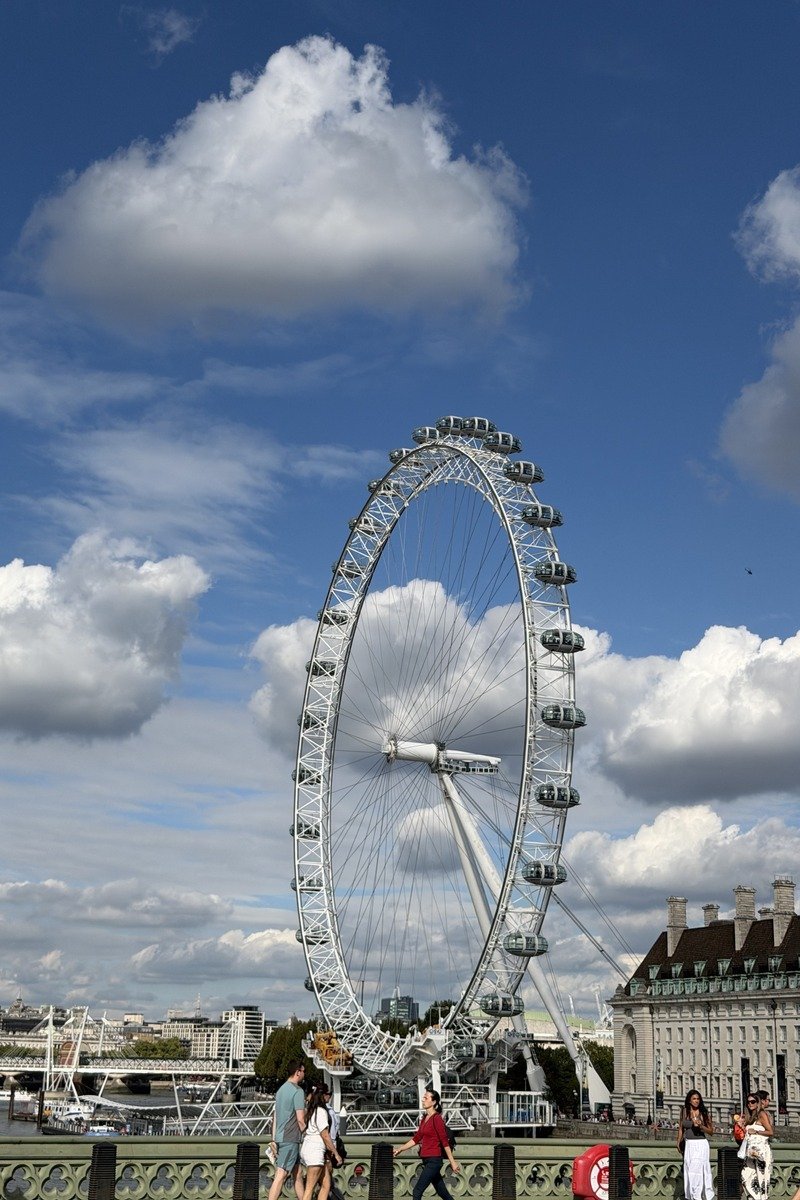 Grande roue panoramique blanche sous un ciel bleu nuageux avec des promeneurs