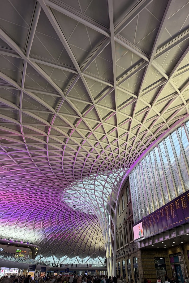 Vaste hall de gare avec toiture géométrique illuminée en violet