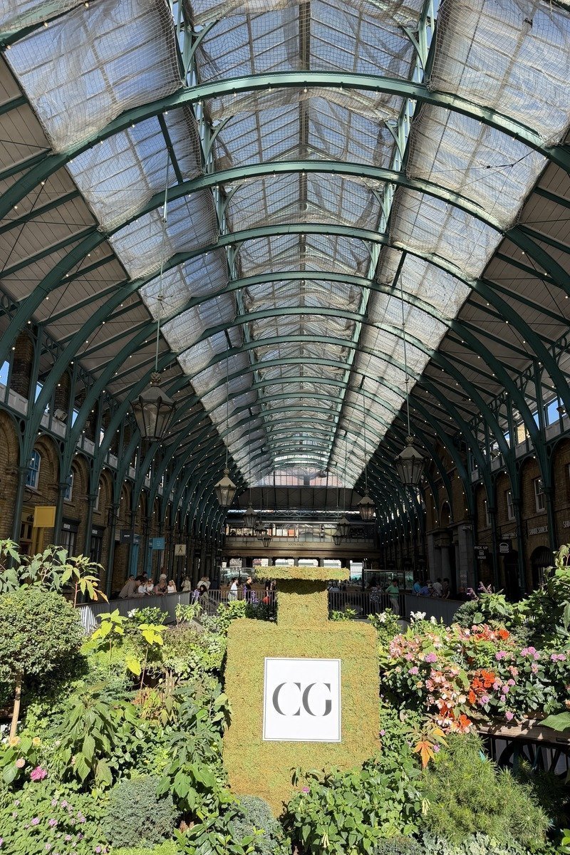 Halle victorienne en fer forgé avec verrière et jardinières fleuries en premier plan