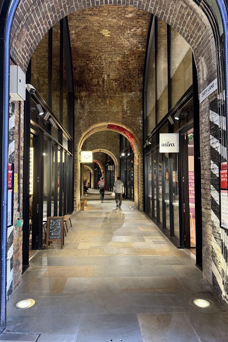 Passage voûté en briques rouges avec boutiques et deux passants