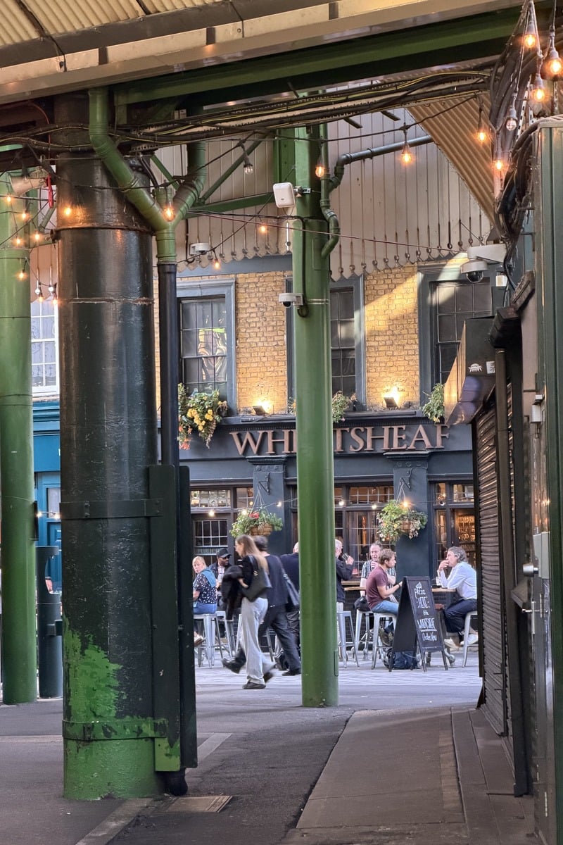 Terrasse animée d'un pub vue entre des colonnes métalliques vertes en soirée