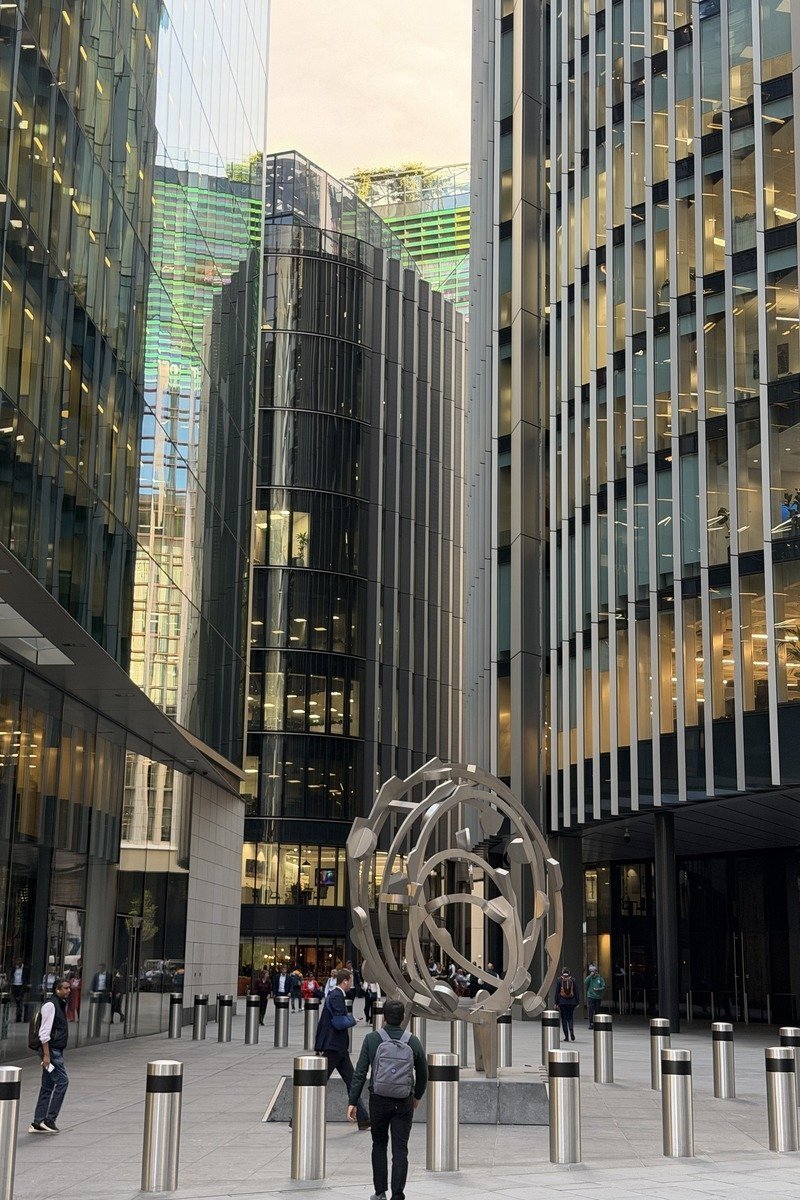Sculpture métallique sphérique sur un parvis entouré de tours en verre